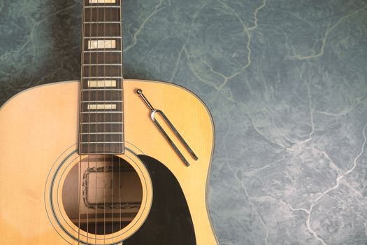 Acoustic guitar on a green marble background, on the guitar there is a tuning fork, music concept.from above view.