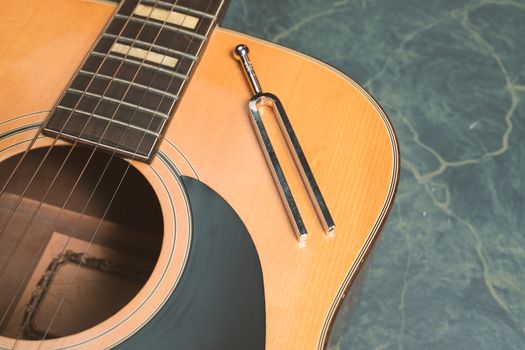 Acoustic guitar on a green marble background, on the guitar there is a tuning fork, music concept.