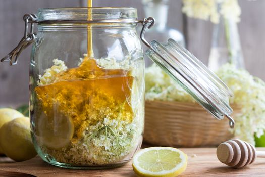 Preparation of a natural elder flower syrup from fresh elder flowers, honey, and lemon - pouring honey into the jar