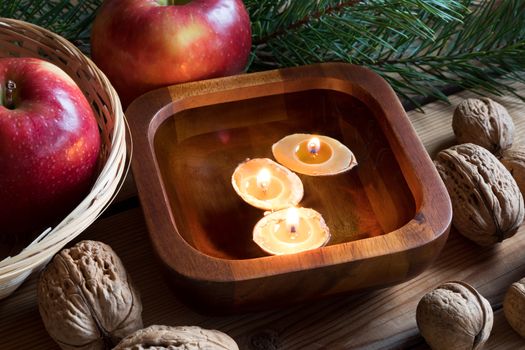 Christmas decoration on a table - apples, pine branches, walnuts and floating candles made from nutshells and beeswax