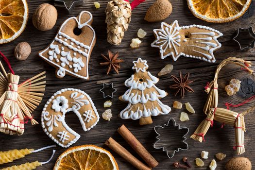 Christmas background with decorated gingerbread cookies, straw ornaments, star anise, walnuts, almonds, nutmeg, cinnamon, frankincense resin, candles made from beeswax and dried orange slices on old wood