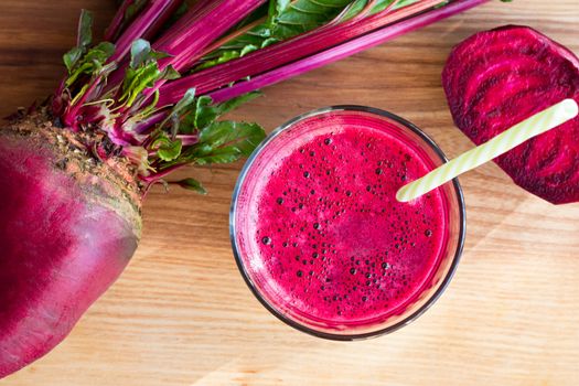 Red beet juice in a glass on a wooden table with fresh beets in the background, top view