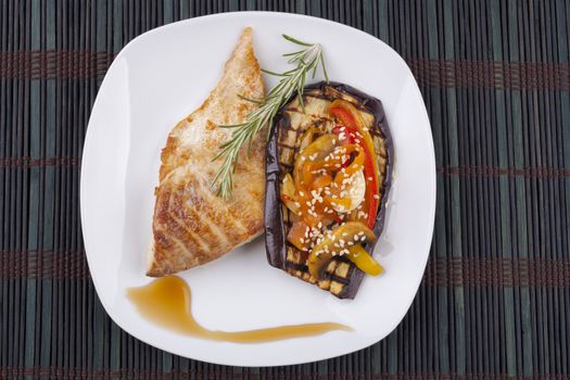 Fish and vegetables on eggplant in white plate on dark background
