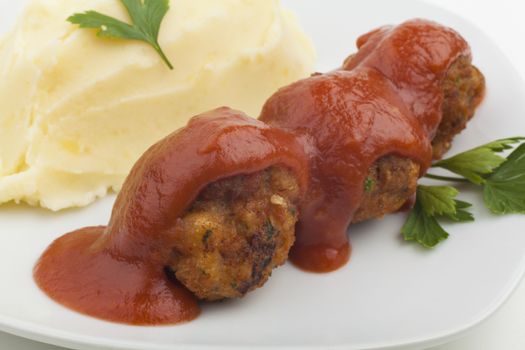 Mushed Potato with meatballs and red sauce on white plate with green parsley 