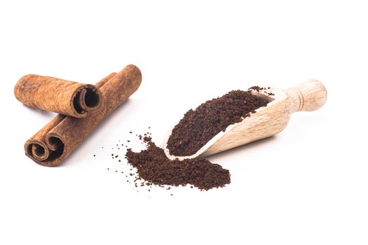 Grounded coffee in wooden spoon and cinnamon sticks isolated on white background