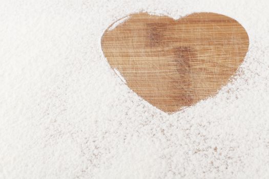 Heart shape flour close-up on brown wood cutting board