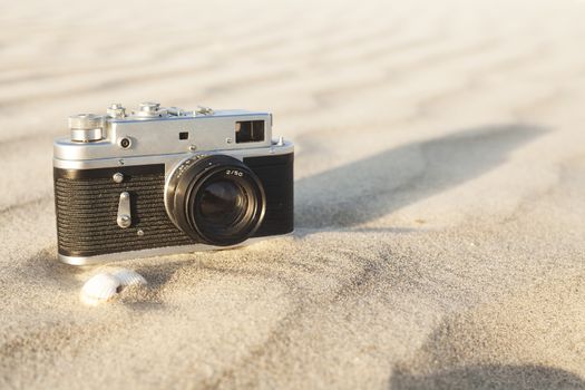 Old camera on sand waves with seachells on sunset lightning