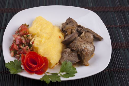 Yellow polenta with stew and tomato salad garnish in white plate on dark wood background