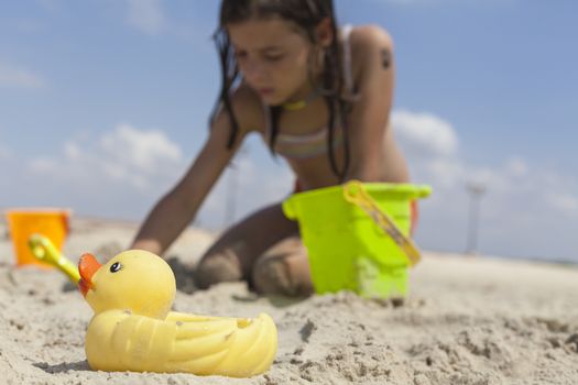 Yellow rubber duck in the sand with child playing in the background