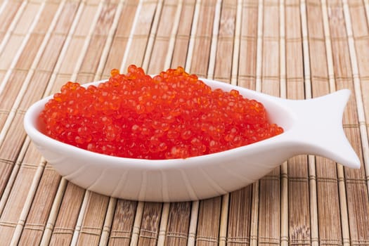 Red caviar in a fish white shape bowl on brown wooden background