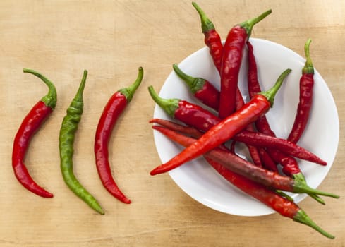 2 chili red peppers and a green one beside a bowl full with red chilis 