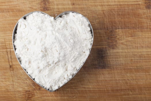Flour shape heart in a mold on brown wood cutting board