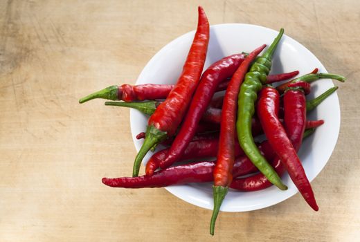 Red chili with one green cilli pepper in a bowl on wood background
