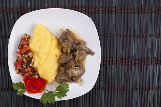 Ornated plate with polenta and tomato flower with parley lieves on dark wood background