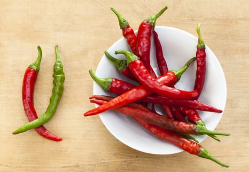Red chili with one green cilli pepper in a bowl on wood background