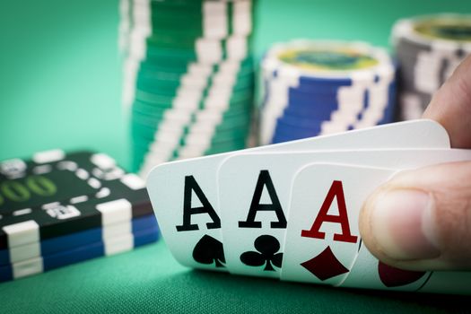 Four aces in a hand with casino chips in the backgroun on green
