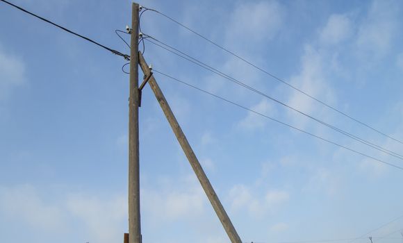 Wooden old 0.4 kV power line support with wires and insulators on blue sky background.