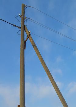 Old wooden support of power transmission lines 0.4 kV with wires and insulators on a blue sky background, vertical image.