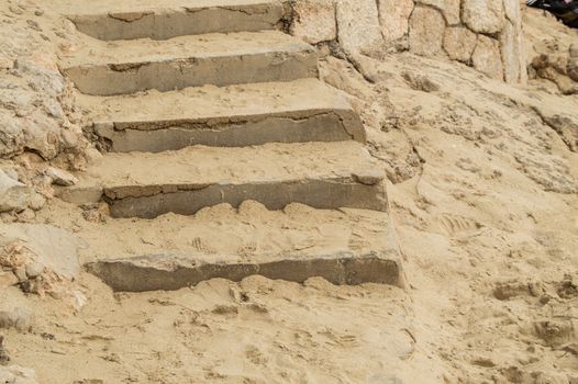 Close-up of stone stairs and sand on the Mediterranean beach, background footprints in the sand.