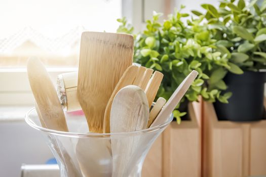 Wooden kitchen utensils in a glass container with a grass in the background. Kitchen interior shot. Home decor and cooking concept