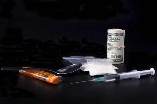 Drugs with a syringe spoon and a lighter beside a lot of dollars on black background 