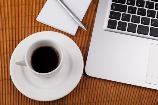 Morning coffee close-up witn laptop pen and white notebook on brown background