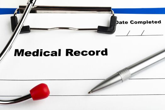 Red stethoscope on  blue clipboard  with medical record close-up with silver colored pen