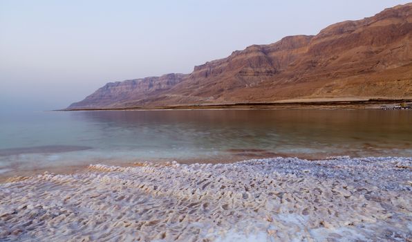 Dead sea lanscape with salt structures on the shore and desert mountains in the background