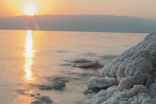 Sunrise in the dead sea with salt formations on the shore