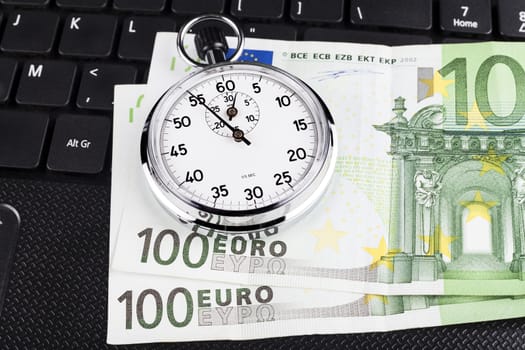 Silver stopwatch on black laptop keyboard with 100 euro bills