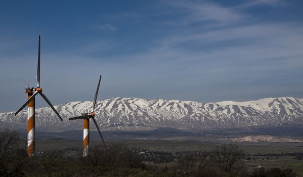 wind turbine farm ona hill with snow mountain peak in the background