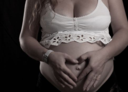 heart shape hands on a pregnant women belly on black background