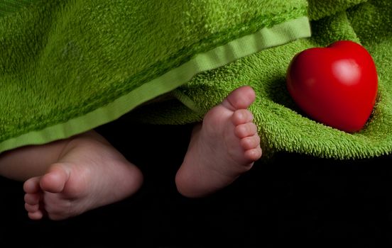 baby feet and a red heart covered with green towel on balck background