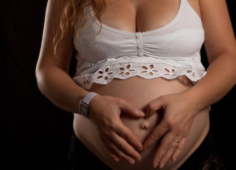 heart shape hands on a pregnant women belly on black background