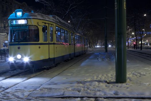 yellow tram in a cold winter night with snow and ice on it