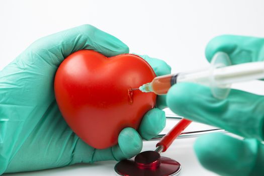 blood drop while injecting red heart with syringe with two hands green gloves