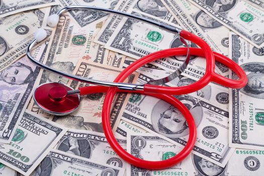 red stethoscope on a pile of dollar bank notes 