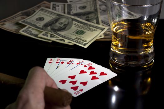 poker playing cards whiskey and some money on a table with reflection