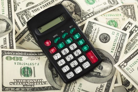 a small black calculator on a pile of dollar bills