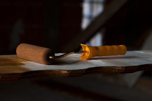 painting roller with yellow handle on a shaped wood plate