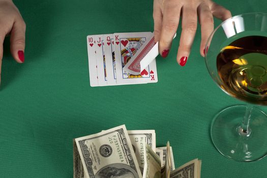 poker cards on green table with dollars and a drink