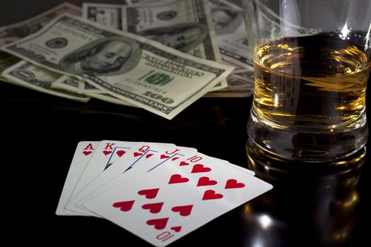 poker playing cards whiskey and some money on a table with reflection