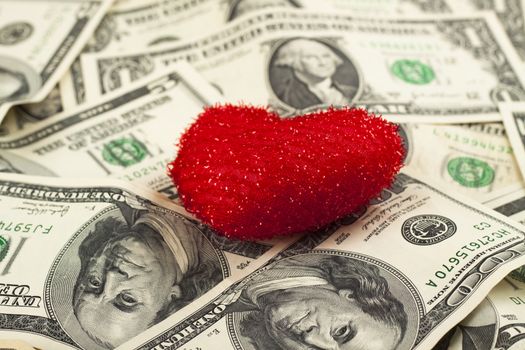 small red toy heart with dollar bills