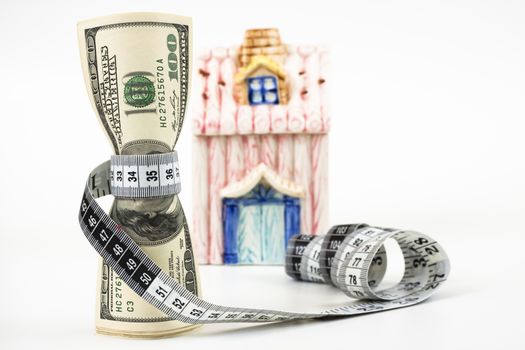 100 dollar bills tight with a measuring tape a small house in the background white background