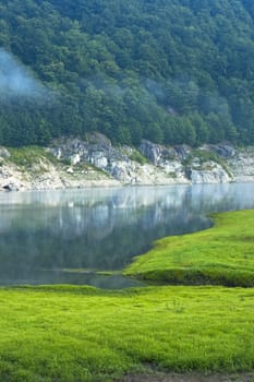 a lake inthe mountains green gras and morning fog