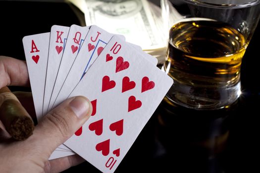 poker playing cards whiskey and some money on a table with reflection