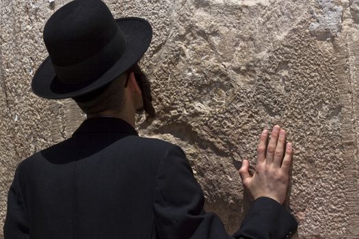 jewish religious man praying at the western wall with one hand on the wall