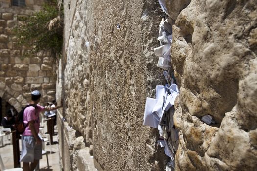 notes in the western wall and a man holding his hand on the wall while praying