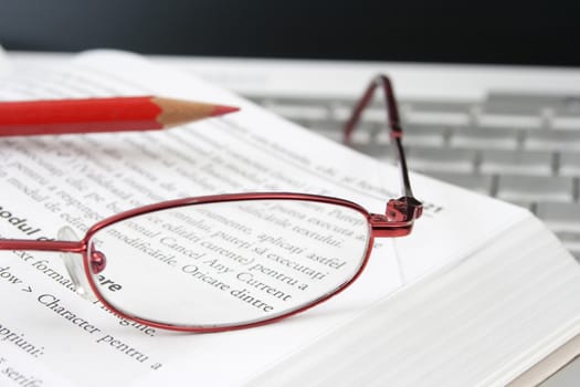 open book on a laptop with a pair of red glasses and a red pencil