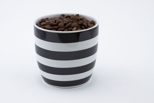 white and black mug full of brown coffee beans on white background